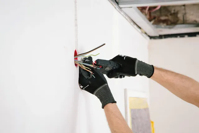 Handwerker in Arbeitshandschuhen schließt Leitungen an einer Wand an