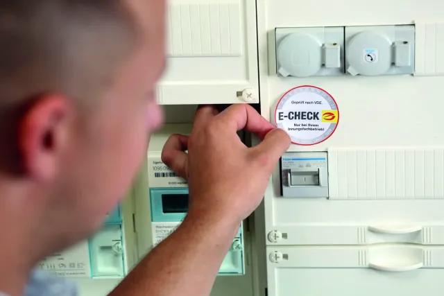 Eine Hand bringt die E-CHECK-Plakette am Zählerschrank an